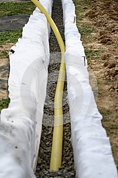 Yellow corrugated pipe with perforation in a trench with crushed stone and geotextile. Drainage works for the removal of