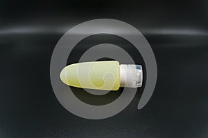 Yellow cosmetic tube of body wash or shampoo on dark background. Travel toiletry silicon bottle