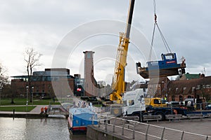 yellow crain lifts blue tug boat called dignity from land into water