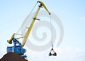 Yellow crane in cargo port translating coal. Industrial scene