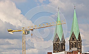Yellow crane in front of two cathedral spires, blue sky, clouds