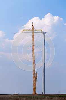 Yellow crane tower placing windmill blade with background of blue sky. Wind Turbine Construction