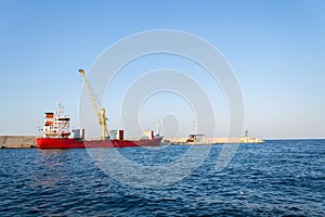 Yellow crane unloading sand from large freighter cargo ship in harbor, freight digitalization, transportation efficiency