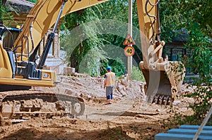 Yellow crawler excavator at a road reconstruction site in a village with old log houses. Summer sunny day.