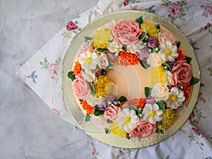 Yellow cream cake decorated with buttercream flowers - peonies, roses, chrysanthemums, carnations - on white wooden background.