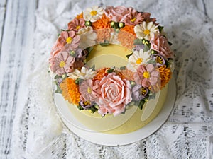 Yellow cream cake decorated with buttercream flowers - peonies, roses, chrysanthemums, scabiosa, carnations - on white wooden back