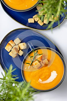 Yellow cream soup and croutons in the blue bowls on the white table