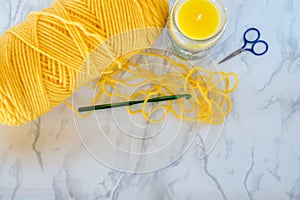 Yellow crochet yarn, hook and scissors with candle on neutral background