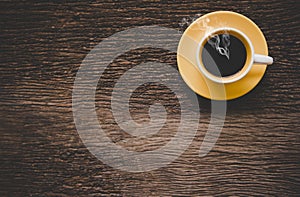 A yellow cup of coffee on old wooden table.