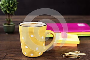 Yellow cup of coffee with white dots. Pretty pink office accessories - notebooks, gold pins, stickers, rubber and polka dot mug