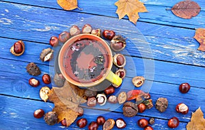 Yellow cup of herbal tea on aged wooden background with fall autumn leaves and chestnuts.