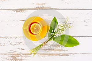 a yellow cup with morning tea with lemon on a white wooden table with a bouquet of spring lily of the neck. morning