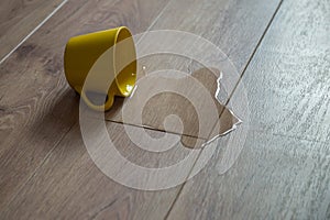 Yellow cup of water spilled on wooden laminate floor. Moisture protection of a floor. Parquet board with spilled water.