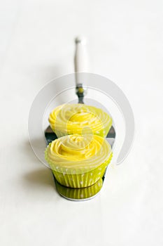 Yellow cupcakes on cake shovel, white background.