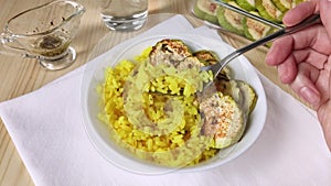 Yellow curry rice and baked zucchini. Hand holds fork with friable rice. Healthy food, cooking spicy vegetables for dinner. Close-