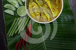 Yellow curry snapper fish with Lotus Stems, Southern Thai Spicy food and fresh vegetable in white dish on banana leaf / selective