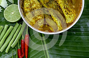 Yellow curry snapper fish with Lotus Stems, Southern Thai Spicy food and fresh vegetable in white dish on banana leaf / selective