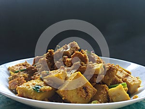 Yellow curry tofu fried on white dish with hot smoke on black background