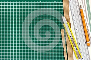 Yellow cutter knife with ruler, pencil and paper sheets on green