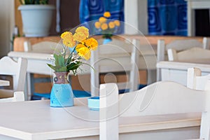 Yellow daisy flowers in blue vase on a table at Greek tavern on Crete island