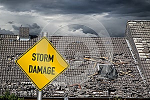 yellow damage warning sign in front of storm damaged roof of house