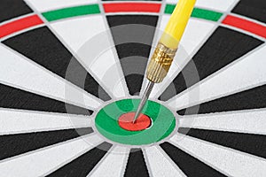 Yellow dart arrow hitting in the target center of dartboard