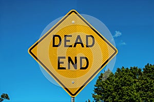 Yellow Dead End Sign against blue sky and some summer trees