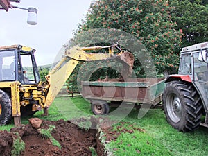 Yellow Digger digging foundations for an extinction to a bungalow with tractor and trailer