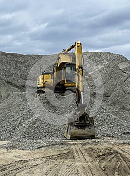 Yellow digger machine on top of a large pile of pebbles and stones