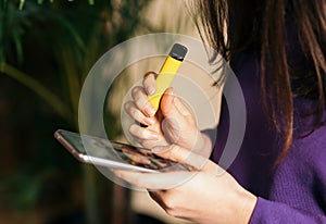 Yellow disposable electronic cigarette in a woman`s hand. Modern online communication