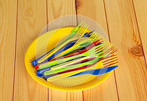 Yellow disposable plates with colored plastic knives, forks.