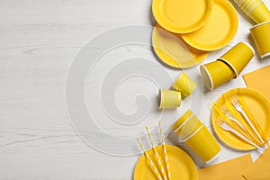 Yellow disposable tableware on white wooden background, flat lay. Space for text