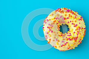 Yellow donut on a blue background with copy space. Multicolor topping on yellow glaze. Unhealthy high-calorie food.