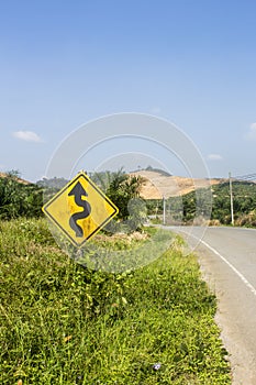 Yellow double curve sign next to a deserted asphalt street. Road trip travel concept. In Phang Nga, Thailand