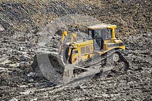 Yellow dozer pushes large piles of dirt