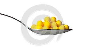 Yellow dragee with vitamins in spoon isolated