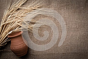 Yellow dry spikelets of wheat on a burlap with a clay pot. Place for text. Still life close up. Top view