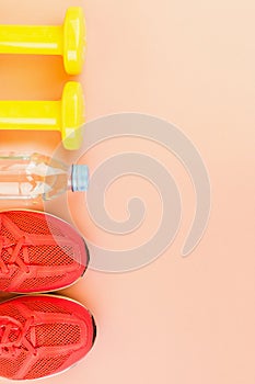 Yellow dumbbells, a bottle of fresh water and pink sneakers