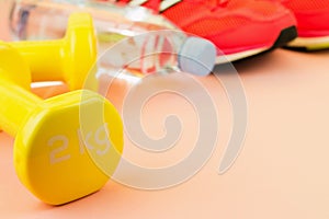 Yellow dumbbells, a bottle of fresh water and pink sneakers