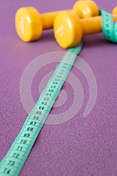 Yellow dumbbells and green measuring tape on fitness mat.
