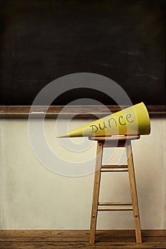 Yellow dunce hat on stool with chalkboard