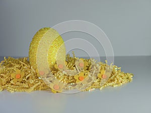 Yellow Easter egg sitting on a bed of yellow paper shreds with little yellow felt flowers on a white background