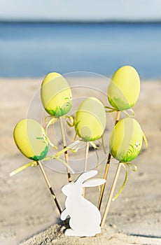 Yellow easter eggs, wooden rabbit are on the beach with sea.