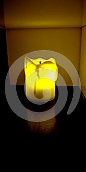 Yellow electric flameless battery powered candle shining in dark cabinet