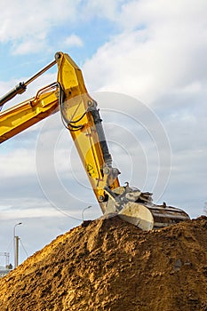 A yellow excavator boom with a bucket digs a pile of earth
