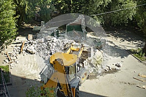 Yellow excavator breaks a brick building in the yard