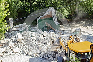 Yellow excavator breaks a brick building in the yard