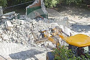 Yellow excavator breaks a brick building in the yard