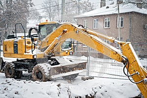 Yellow excavator covered by snow at winter construction site