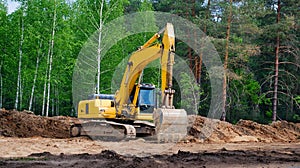 Yellow excavator with a crawler on a caterpillar track, works on the construction of a highway